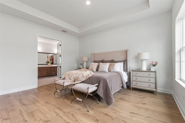 bedroom featuring a raised ceiling, connected bathroom, and light hardwood / wood-style flooring