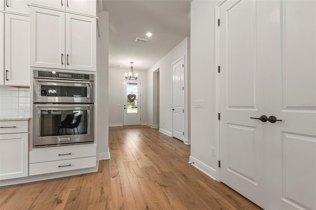 kitchen featuring white cabinets, decorative backsplash, double oven, and a notable chandelier