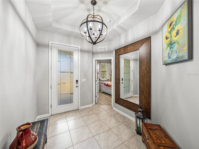 entryway featuring light tile patterned floors, a notable chandelier, a tray ceiling, and a textured ceiling