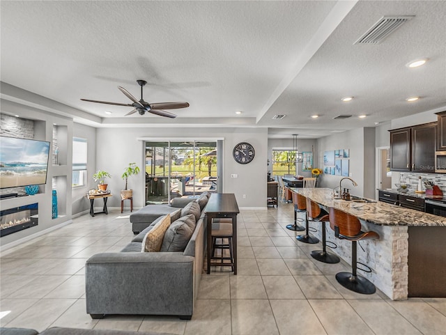 living room featuring sink, a textured ceiling, a raised ceiling, ceiling fan, and light tile patterned floors