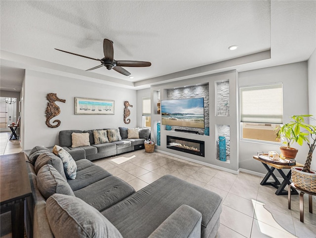 living room with ceiling fan, a raised ceiling, light tile patterned flooring, and plenty of natural light