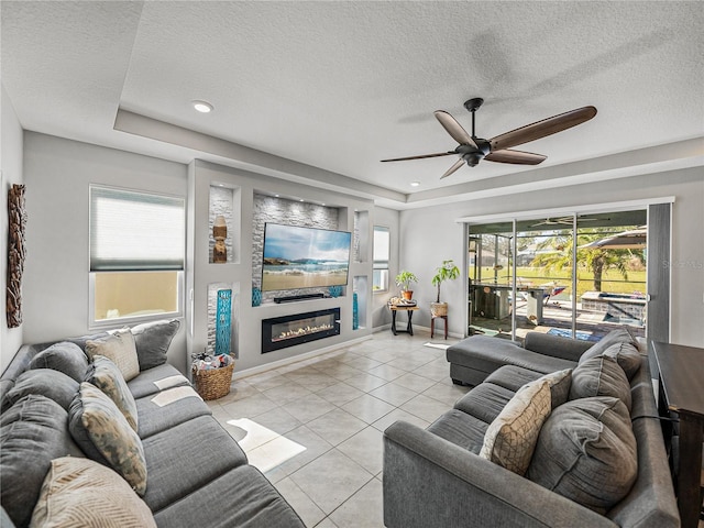 living room with a textured ceiling, ceiling fan, a raised ceiling, and light tile patterned floors