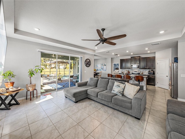 living room with light tile patterned flooring, ceiling fan, and a tray ceiling