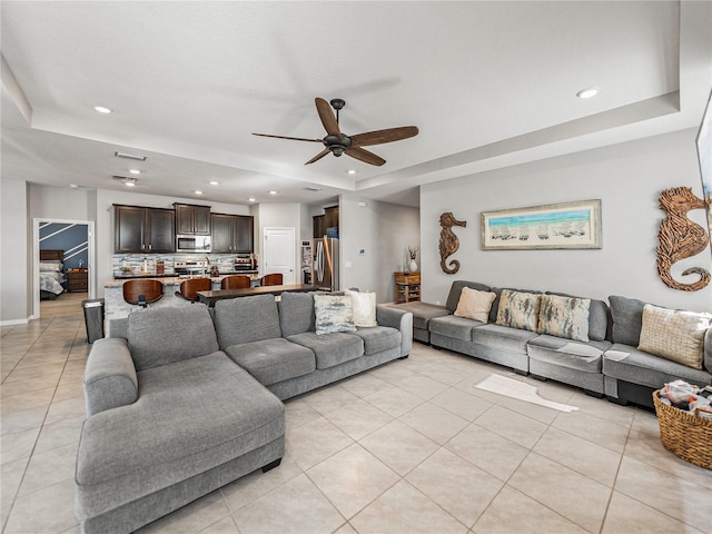 living room featuring ceiling fan, a tray ceiling, and light tile patterned floors