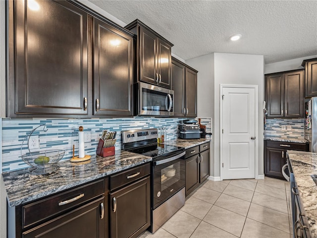 kitchen featuring dark stone countertops, stainless steel appliances, decorative backsplash, dark brown cabinetry, and light tile patterned flooring