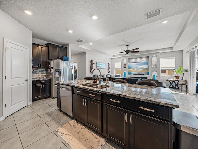 kitchen with a raised ceiling, a kitchen island with sink, appliances with stainless steel finishes, ceiling fan, and sink