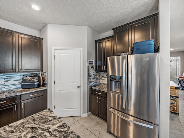 kitchen with stainless steel refrigerator with ice dispenser, light tile patterned flooring, backsplash, and dark stone counters