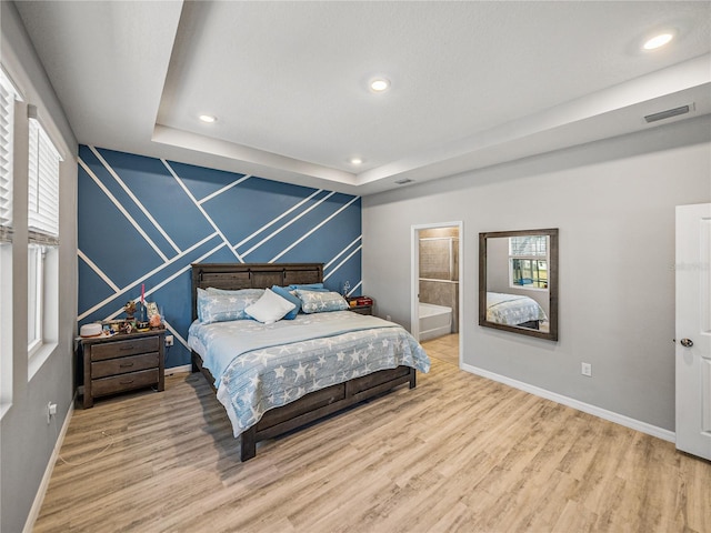 bedroom with ensuite bathroom, a raised ceiling, and wood-type flooring