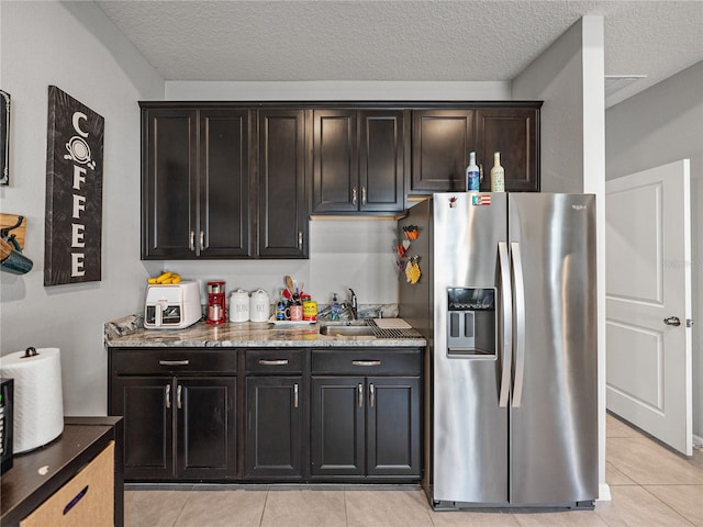 kitchen featuring sink, a textured ceiling, light tile patterned flooring, light stone countertops, and stainless steel refrigerator with ice dispenser