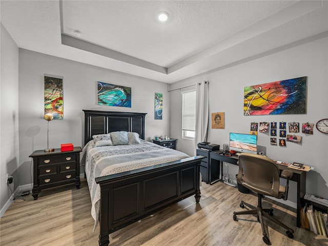 bedroom with light hardwood / wood-style floors, a textured ceiling, and a tray ceiling