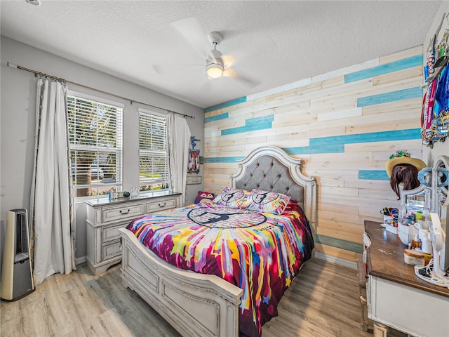 bedroom featuring ceiling fan, light hardwood / wood-style floors, wooden walls, and a textured ceiling