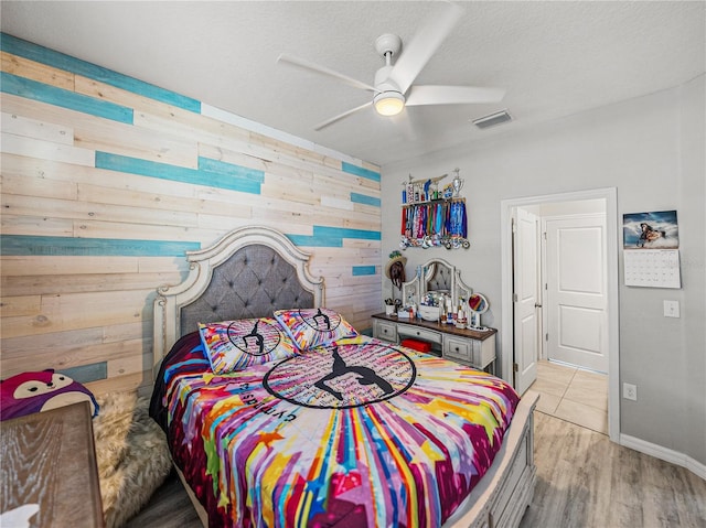 bedroom featuring a textured ceiling, ceiling fan, light hardwood / wood-style floors, and wooden walls