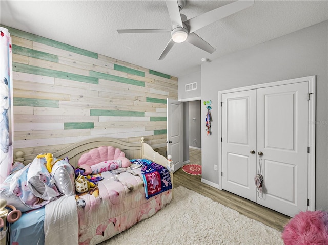 bedroom featuring a closet, wood-type flooring, ceiling fan, wooden walls, and a textured ceiling