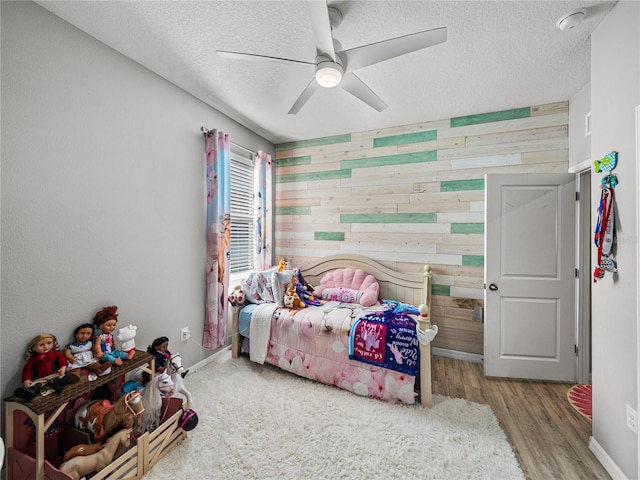 bedroom featuring a textured ceiling, ceiling fan, wooden walls, and light hardwood / wood-style flooring