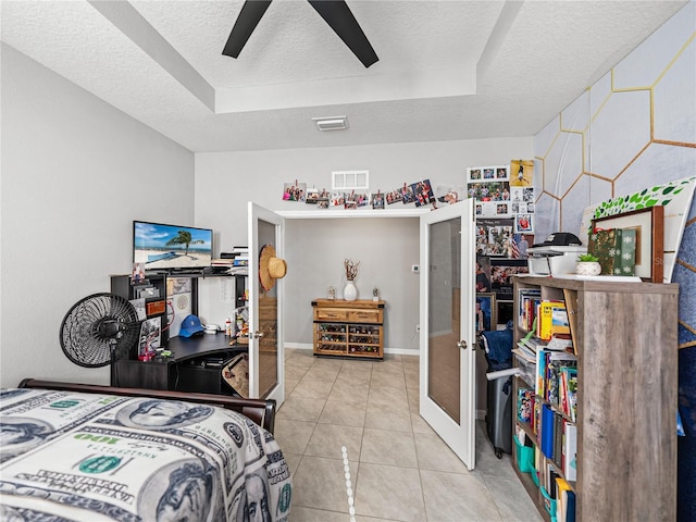 tiled bedroom with ceiling fan, french doors, a textured ceiling, and a tray ceiling