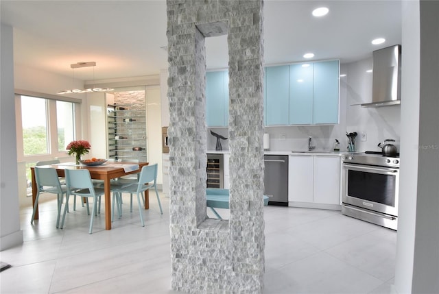 kitchen featuring tasteful backsplash, white cabinetry, hanging light fixtures, stainless steel appliances, and wall chimney range hood