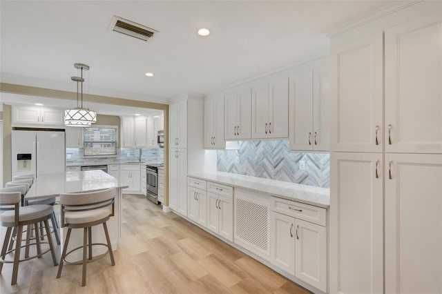 kitchen with pendant lighting, light stone countertops, tasteful backsplash, white cabinetry, and stainless steel appliances