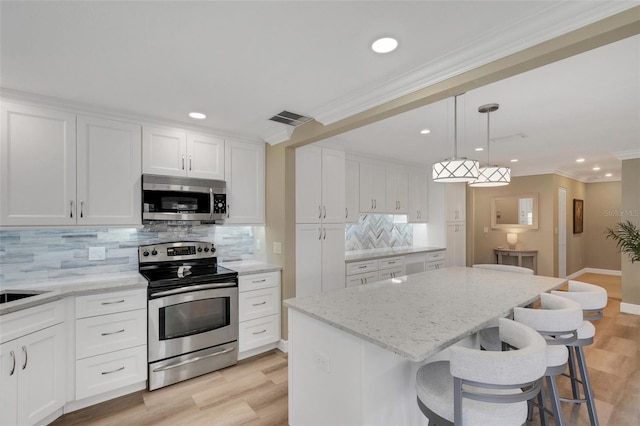 kitchen with white cabinets, decorative backsplash, a kitchen island, and appliances with stainless steel finishes