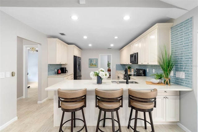 kitchen featuring a breakfast bar, light wood-type flooring, kitchen peninsula, and black appliances