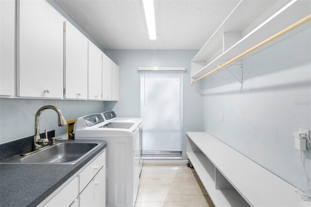 laundry area featuring cabinets, washing machine and dryer, sink, and a textured ceiling