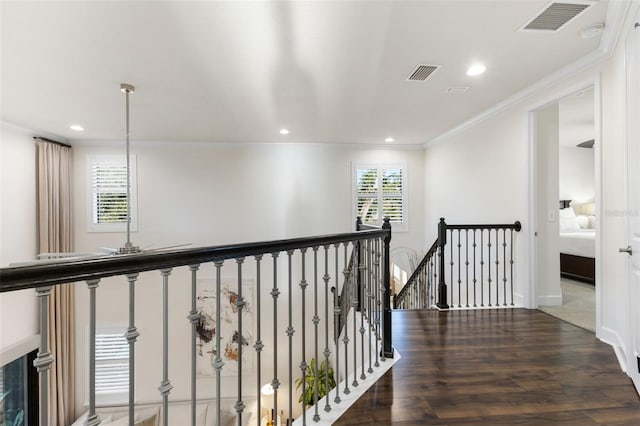 corridor with wood finished floors, visible vents, an upstairs landing, and ornamental molding