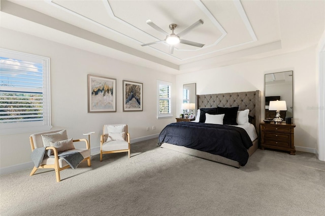 bedroom featuring a raised ceiling, light colored carpet, baseboards, and ceiling fan