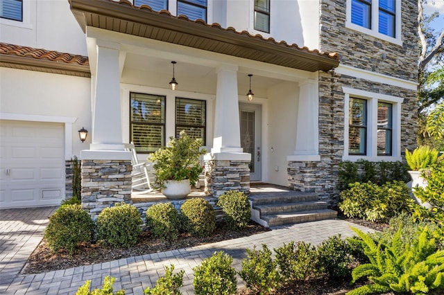 property entrance with a tiled roof, covered porch, stucco siding, a garage, and stone siding