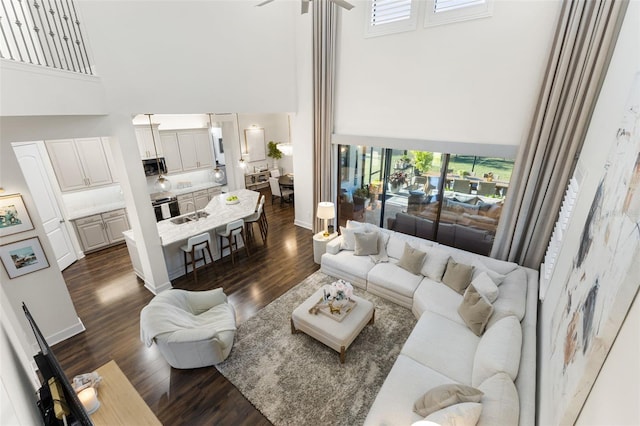 living area featuring baseboards, a towering ceiling, and dark wood-style flooring