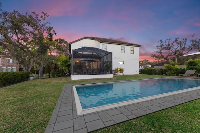 pool at dusk with a lanai, a yard, fence, and an outdoor pool