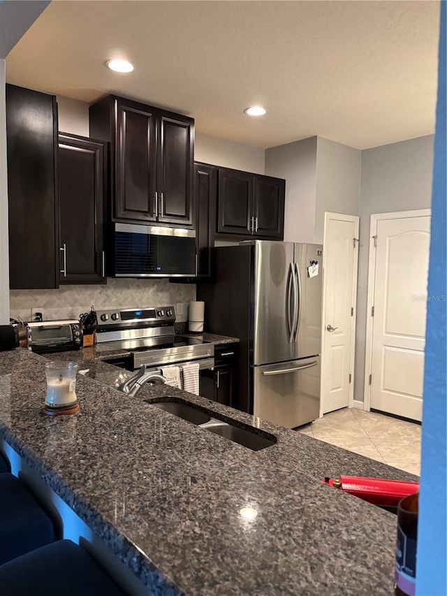 kitchen with sink, backsplash, dark stone countertops, light tile patterned floors, and appliances with stainless steel finishes