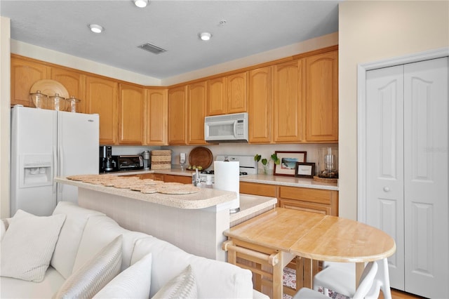 kitchen featuring white appliances, a kitchen bar, and a center island with sink