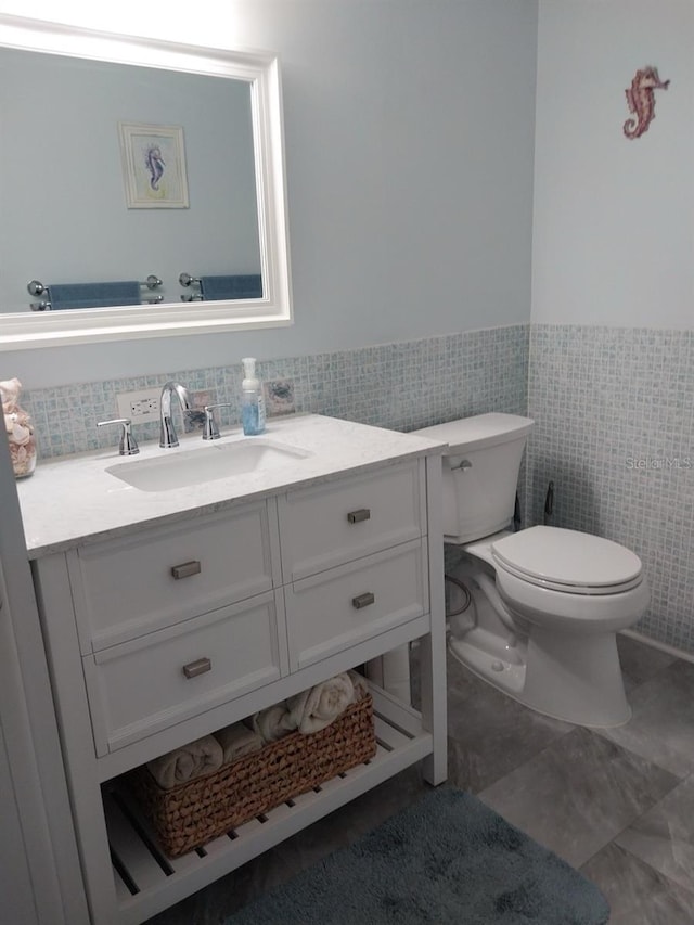 bathroom with tile patterned floors, vanity, toilet, and tile walls