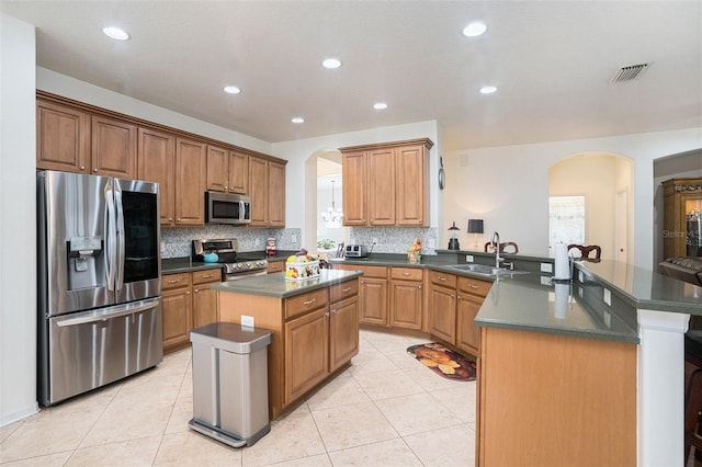 kitchen with appliances with stainless steel finishes, an island with sink, sink, light tile patterned floors, and kitchen peninsula