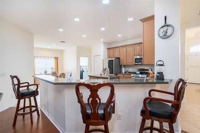 kitchen featuring sink, a breakfast bar area, appliances with stainless steel finishes, decorative backsplash, and kitchen peninsula