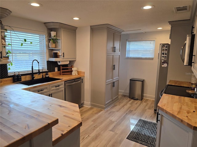 kitchen with dishwasher, sink, wooden counters, light hardwood / wood-style floors, and gray cabinets