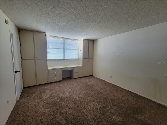 unfurnished bedroom featuring built in desk, carpet, and a textured ceiling