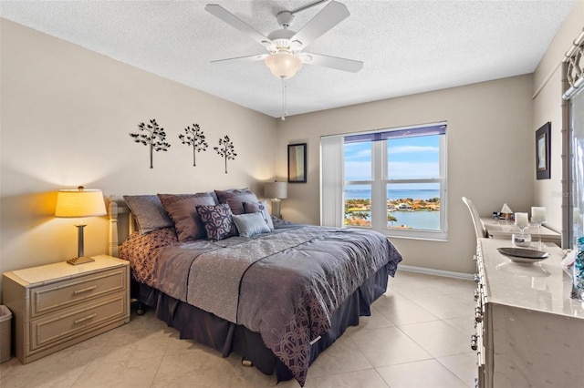 bedroom featuring a textured ceiling, a water view, ceiling fan, and light tile patterned flooring