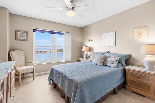 tiled bedroom featuring ceiling fan, a water view, and a textured ceiling