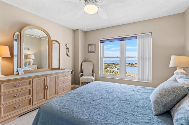 bedroom featuring ceiling fan, a water view, and a textured ceiling