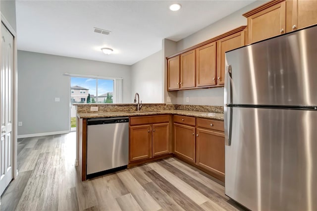 kitchen featuring light stone countertops, sink, stainless steel appliances, and light hardwood / wood-style floors