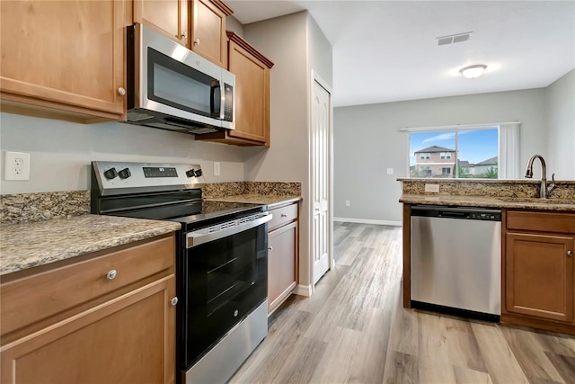 kitchen with appliances with stainless steel finishes, light hardwood / wood-style floors, light stone counters, and sink