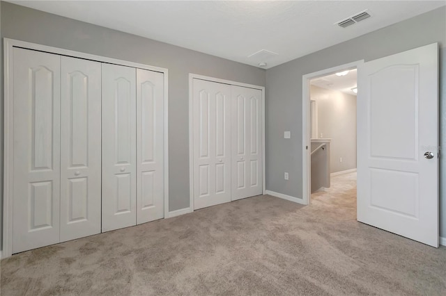 unfurnished bedroom featuring light carpet and two closets