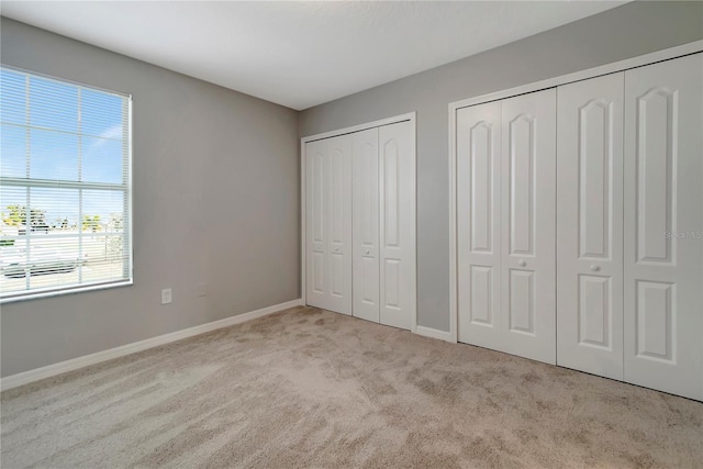 unfurnished bedroom featuring light carpet and two closets