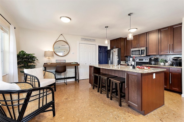 kitchen with appliances with stainless steel finishes, dark brown cabinets, a center island with sink, and hanging light fixtures