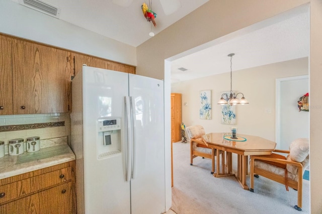 kitchen featuring a chandelier, light carpet, pendant lighting, and white refrigerator with ice dispenser