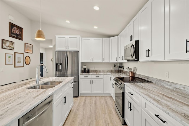 kitchen with sink, light stone counters, vaulted ceiling, white cabinets, and appliances with stainless steel finishes