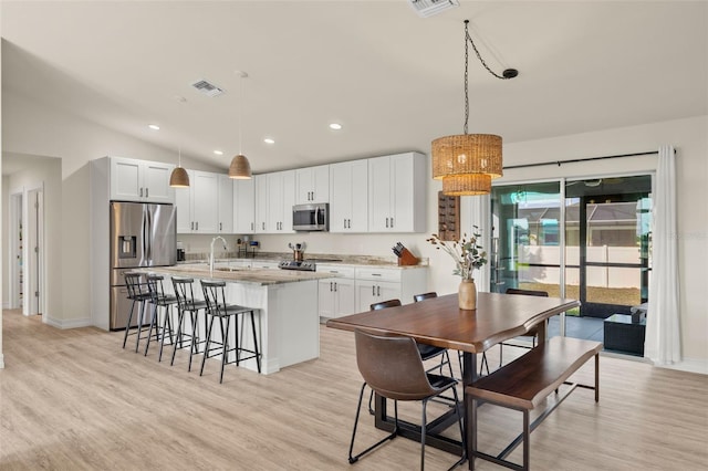 kitchen featuring appliances with stainless steel finishes, light stone counters, pendant lighting, a center island with sink, and white cabinets