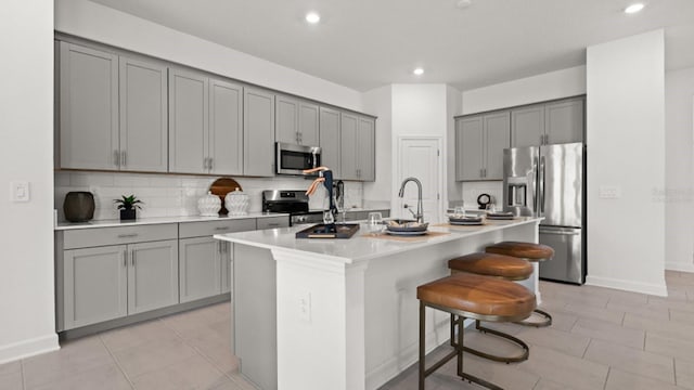 kitchen with stainless steel appliances, a kitchen island with sink, a breakfast bar area, and gray cabinetry