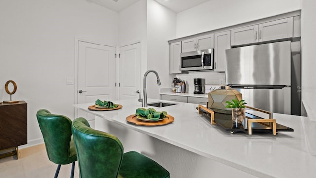 kitchen featuring kitchen peninsula, a breakfast bar, stainless steel appliances, sink, and gray cabinets