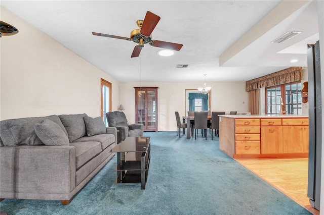 carpeted living room featuring ceiling fan with notable chandelier